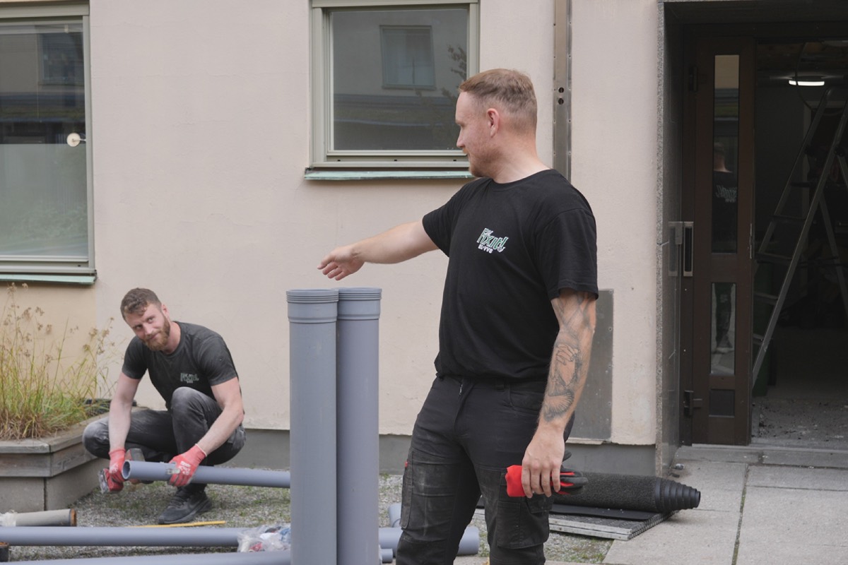 Två av Fixits montörer med avloppsrör på gården utanför ett flerbostadshus